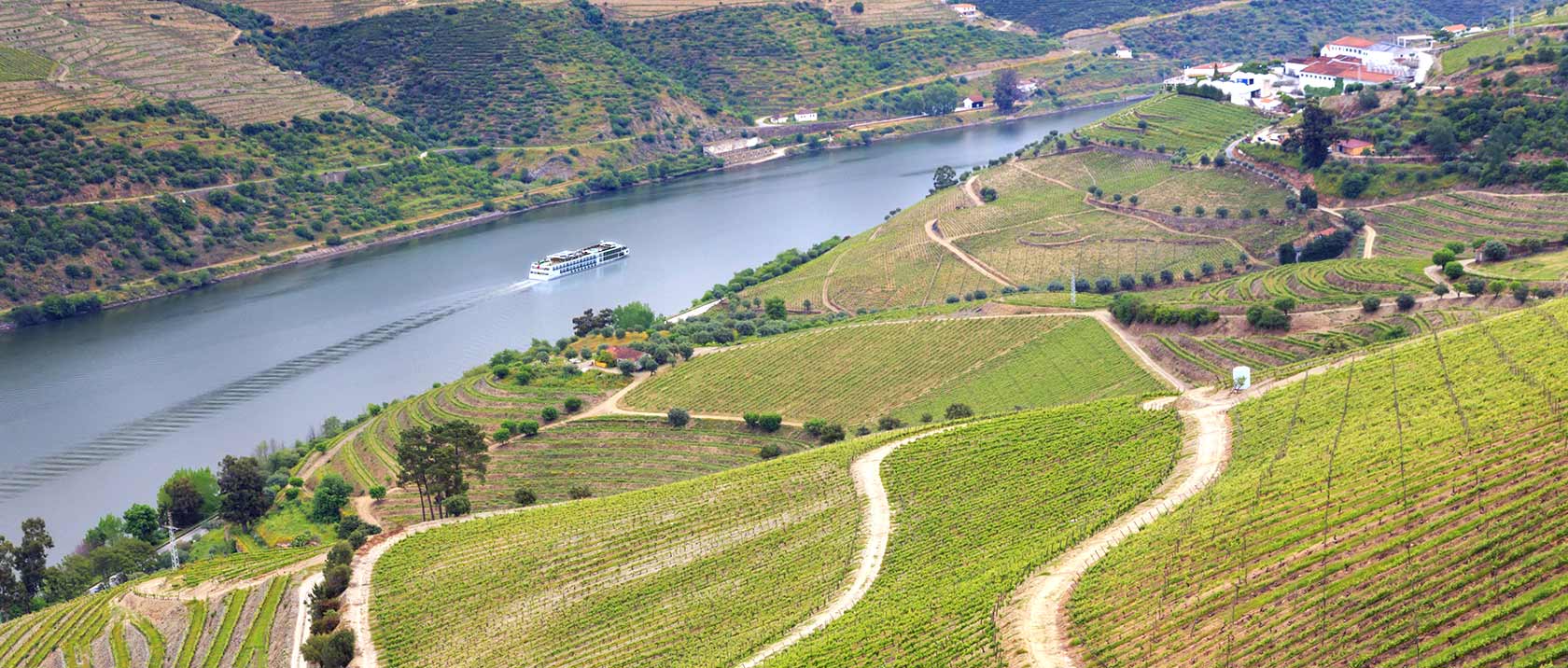 A Viking River Ship sailing down the Duoro as seen from a mountainside of green vineyards.